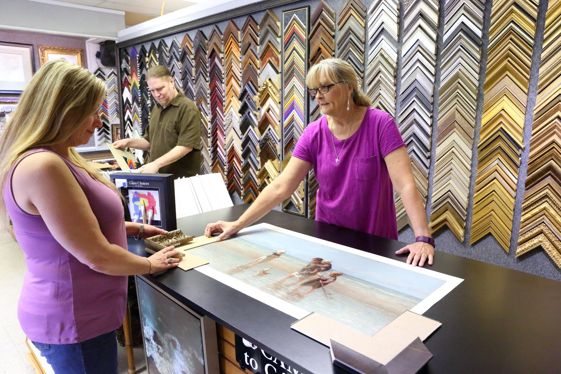 My Workshop staff consulting with a customer at the counter, choosing a moulding sample in front of a full wall of frame corners